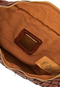 Interno di una borsa in pelle marrone con una fodera in tessuto testurizzato. Presenta una cerniera in metallo e un'etichetta in pelle rettangolare con testo in rilievo e un'etichetta.