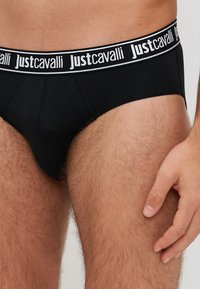 Czarne figi wykonane z miękkiego materiału z białym logo "Justcavalli" na pasku. Posiadają dopasowany kształt i elastyczne materiały zapewniające komfort.