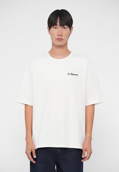 Witte katoenen t-shirt met korte mouwen en een ronde halslijn. Bevat zwarte geborduurde tekst "Les Benjamin" op de linkerborst.
