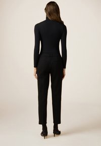 Černý přiléhavý rolák spárovaný s černými kalhotami s vysokým pasem. Outfit má elegantní design s hladkou texturou a přizpůsobeným střihem.