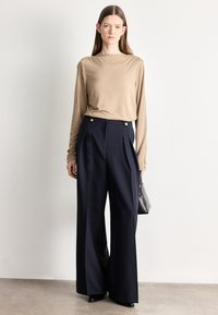 Beżowa bluzka z długim rękawem i okrągłym dekoltem w połączeniu z granatowymi, szerokimi spodniami z wysokim stanem, ozdobionymi złotymi guzikami.