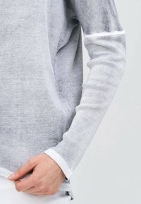 Grå ribbad långärmad topp med vit detalj vid ärmsluten och nederkant, med en avslappnad passform och mjuk textur.