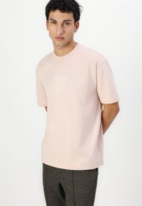 Light pink cotton t-shirt featuring "GUESS CALIFORNIA L.A. Est.1981" printed in white. Short sleeves and a crew neckline.