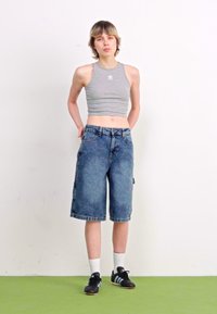 Top corto gris y pantalones cortos de mezclilla azules hasta la rodilla con un ajuste relajado, que cuentan con bolsillos laterales y costuras de contraste. Zapatillas negras con detalles blancos.