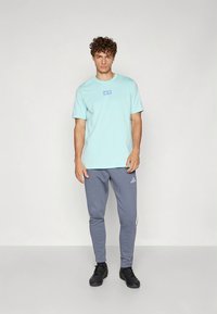 Hellblaues Baumwoll-T-Shirt mit kurzen Ärmeln und kleinem Logo auf der Brust, kombiniert mit grauen Sweatpants mit Seitenstreifen und Logo.