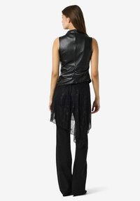 Svart läder ärmlös topp med hög krage, i kombination med genomskinlig svart spetsöverdel och lösa svarta byxor med asymmetrisk nederkant.