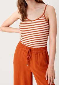 Pruhovaný bezrukávový top v krémové a rezavé barvě, se výstřihem do V a tenkými ramínky. Spárován s rezavými kalhotami na šňůrku s texturovanou látkou.