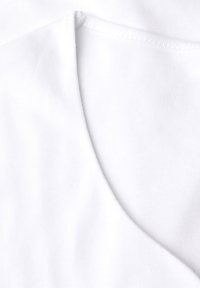 Weißer Baumwollstoff mit einem V-Ausschnitt-Design und glatter Textur. Das Bild zeigt Nähte und dezente Faltendetails.