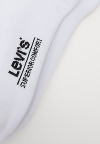 Chaussettes en coton blanc ornées d'un logo Levi's noir brodé et du texte "Supermarine". La texture semble lisse avec des détails en côtes.