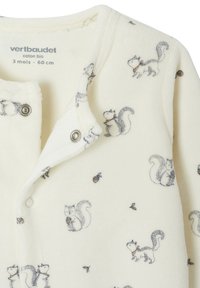 Baby-Overall aus Bio-Baumwolle mit Druckknöpfen, versehen mit einem Muster von verspielten Eichhörnchen und kleinen Eicheln auf cremefarbenem Stoff.
