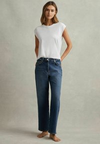 Vit kortärmad t-shirt matchad med högmidjade, raka mörkblå jeans, med traditionell femficksdesign och knäppning.