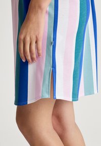 Abito a righe multicolori con tonalità di blu, rosa e teal. Tessuto morbido, lunghezza al ginocchio con uno spacco laterale e orlo arrotondato.