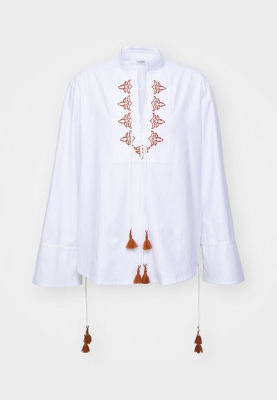 Blusa di cotone bianca con scollo rotondo, caratterizzata da dettagli ricamati arancioni e frange sul davanti, maniche lunghe con polsini larghi.