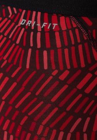 Czerwono-czarne legginsy sportowe z etykietą DRI-FIT. Tkanina ma teksturowany wzór naprzemiennych czerwonych linii na ciemnym tle.