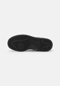 Semelle extérieure en caoutchouc noir avec un motif de traction texturé. Présente un logo circulaire et un design de semelle distinct pour une meilleure adhérence.