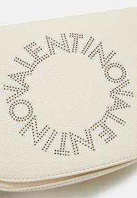 Valkoinen nahkalaukku, jossa on rei'itetty ympyräkirjoituskuvio. Silkkinen pinta, jossa on hienovaraiset ompeleet reunoilla.