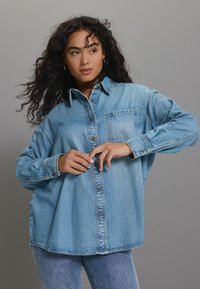 Lichtblauw denim overhemd met een knoopsluiting aan de voorkant, kraag en een enkele borstzak. Het heeft lange mouwen en een relaxte pasvorm.
