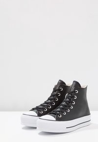 Czarne sneakersy typu high-top wykonane ze skóry, z białą gumową podeszwą, okrągłym noskiem i czarnymi sznurówkami, zdobione srebrnymi oczkami i teksturowanym wykończeniem.