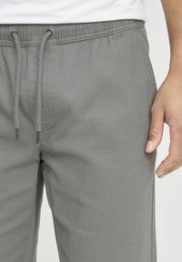 Light grey jogger pants made of soft fabric, featuring an elastic waistband with drawstring, side pockets, and straight leg design.