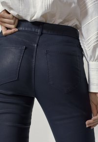 Marinblå tajta jeans med en slät textur, med två bakfickor och hög midja, i kombination med en vit plisserad skjorta.