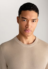 Maglione beige a coste con scollatura tonda, design aderente e tessuto testurizzato. Finitura liscia con dettagli sottili.