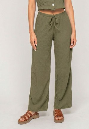Femme portant un pantalon large texturé vert olive avec une taille à cordon et des sandales à larges brides marron.