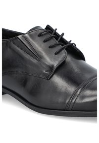 Czarne skórzane buty wizytowe z gładkim wykończeniem, zamkniętym systemem sznurowania i subtelnymi detalami przeszycia wzdłuż boku oraz czubka.