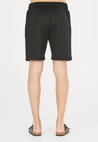 Svarta sportshorts med elastisk midja, slät textur, midjekort längd och minimala sömnadsdetaljer. Bärs med sandaler med öppen tå.