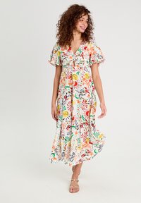 Robe midi florale à manches bouffantes courtes, avec un devant à nouer, présentant des motifs vifs en rose, jaune et vert sur un fond blanc.