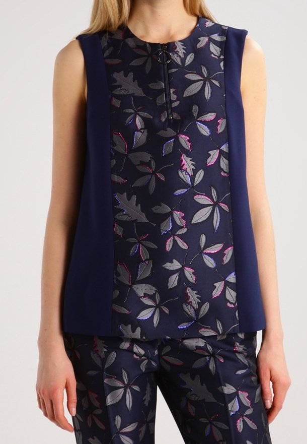 Haut sans manches bleu marine avec un motif floral central en gris, rose et violet, associé à un pantalon à imprimé floral assorti sur une personne debout.