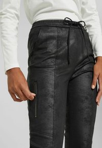 Black faux leather pants with a drawstring waist, featuring a zippered side pocket, smooth texture, and subtle sheen.