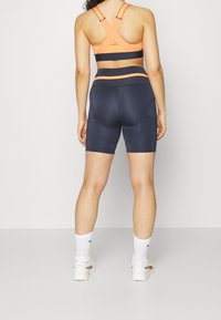 Sportbh i orange och svart med korsade axelremmar, kombinerad med mörkblå tajta shorts med sidofickor och en slät textur.