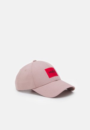 Light pink baseball cap with curved brim and red rectangular patch displaying "HUGO" in black letters.
