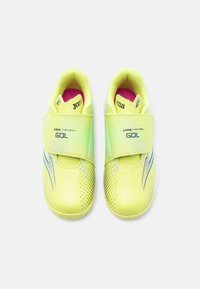 Ζευγάρι παιδικά αθλητικά παπούτσια νέον κίτρινου χρώματος με λουριά βέλκρο, μαύρες λεπτομέρειες λογότυπου και ροζ εσωτερικές σόλες, τοπθετημένα σε λευκό φόντο.