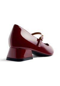 Scarpa Mary Jane in vernice rossa con tacco basso e spesso e una sottile cinturino con fibbia dorata. Finitura liscia e lucida, punta arrotondata.