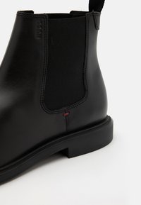 Schwarze Leder-Chelsea-Stiefel mit elastischem Seitenpanel, runder Zehenform, kontrastierendem roten Nähten und flacher Gummisohle. Minimalistisches Design.