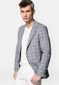 Szary w kratę żakiet o dopasowanym kroju, wykonany z fakturowanej tkaniny, z wyciętym kołnierzem i czarnymi guzikami. Noszony na białym swetrze z dekoltem w serek.