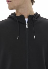 Felpa nera con zip, dalla texture liscia, dotata di cappuccio con cordoncino e hardware della cerniera in argento. Design semplice, senza fantasie né dettagli.