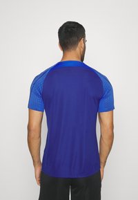 Camisa atlética de hombre de manga corta; cuenta con un cuerpo azul marino sólido y acentos en el hombro de un patrón azul texturizado. Tejido ligero.