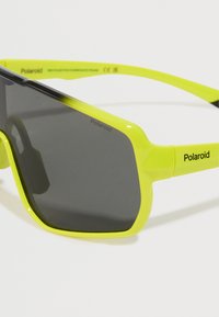 Γυαλιά ηλίου Polaroid με φωτεινό κίτρινο σκελετό και σκούρους γκρι φακούς. Διαθέτουν τετράγωνο σχήμα και γυαλιστερή φινίρισμα. Έχει branding στα χέρια.