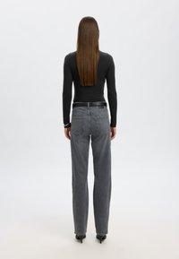 Juodas ilgas rankovės marškinėliai derinami su aukšto liemens pilkais platesniais džinsais. Džinsai turi galinę kišenę ir tekstūruotą medžiagą.