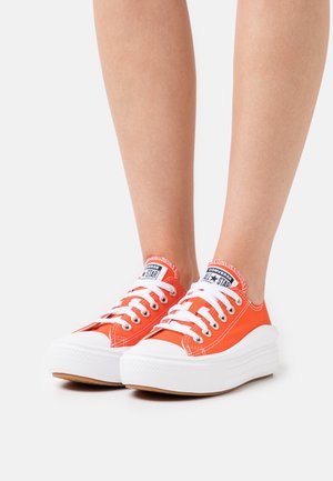 Orangefarbene Canvas-Sneaker mit weißen Gummisohlen und Schnürsenkeln, mit rundem Zehenbereich und schwarzem Logoaufnäher auf der Zunge.