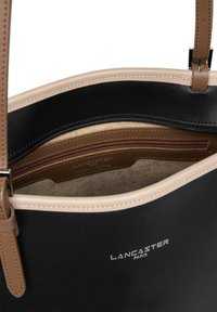 Sac fourre-tout noir avec des accents en cuir beige, texture lisse, compartiment zippé et détail de logo intérieur en brun.