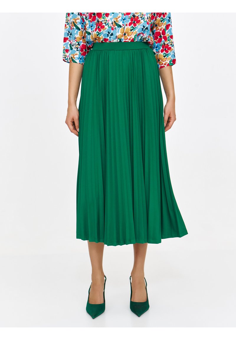 Zielona plisowana spódnica z wysokim stanem, zestawiona z zielonymi czółenkami na szpic. Bluzka w kwiatowy wzór z krótkimi rękawami. Gładki, zwiewny materiał.