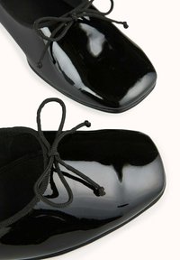 Ballerines en cuir verni noir avec un embout carré, ornées d'un nœud en dentelle noire et d'une doublure intérieure douce. Fini lisse et brillant.