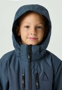 Giacca impermeabile blu navy con colletto alto, cappuccio regolabile e cerniere frontali. Presenta il logo e due tasche sul petto, con una texture liscia.