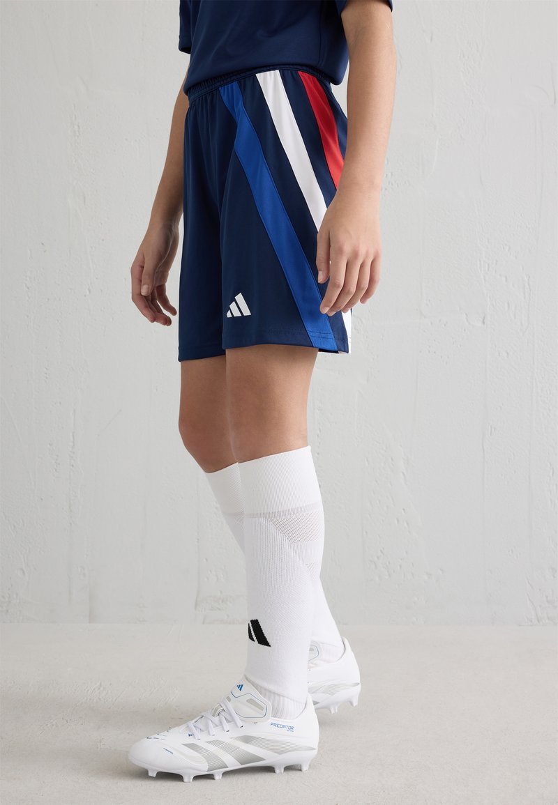 Námořnické modré sportovní šortky s diagonálními pruhy v modré, červené a bílé barvě. Kombinujte s bílými crew ponožkami a bílými kopačkami s modrými akcenty.