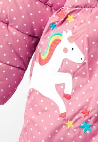Chaqueta acolchada rosa con lunares blancos, un diseño de unicornio bordado y acentos coloridos de estrellas en azul, amarillo y rojo.