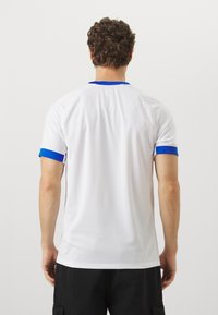 Maglia sportiva bianca con accenti blu sul colletto e sulle maniche, realizzata in un tessuto texturizzato e dal design a vestibilità regolare.