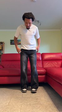 Pantalones de mezclilla negros acampanados con un acabado desgastado, combinados con una camiseta blanca sencilla y zapatillas en blanco y negro, de pie sobre un suelo de baldosas.